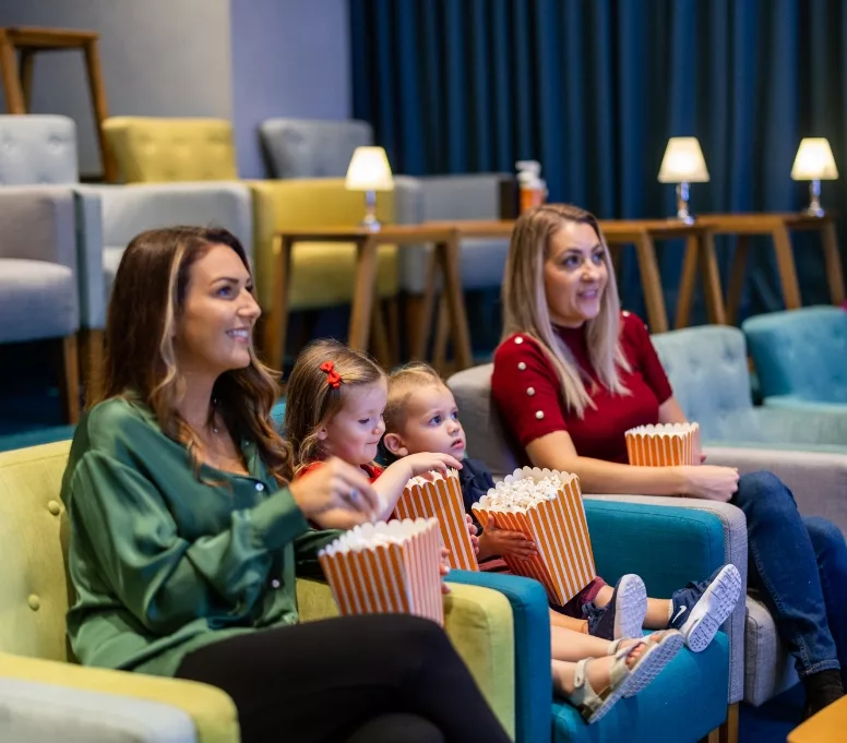 Two women and two children enjoying a movie with popcorn.