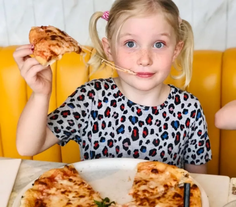 A child eating a piece of pizza with stretching cheese.
