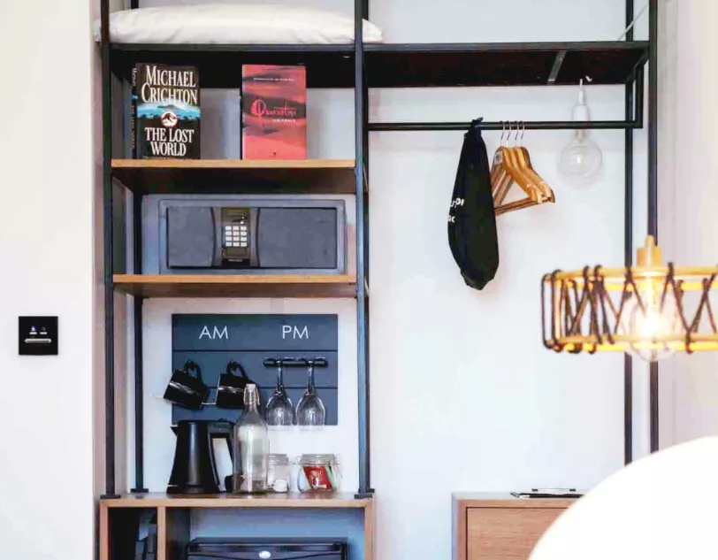 Hotel room shelves containing mugs, a kettle, hangers and books.