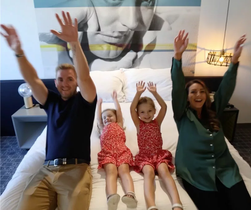 A couple and their two kids jumping onto a bed.