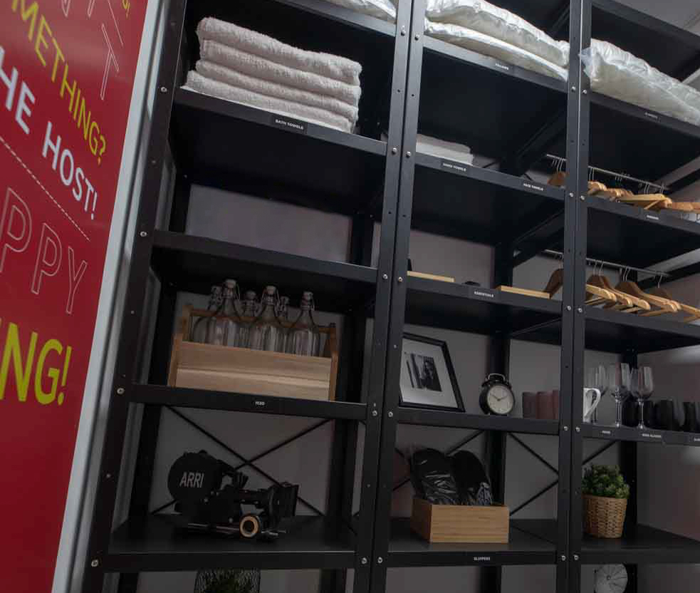 A closet with tall shelves containing towels, water bottles and clothes hangers.